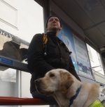 A man with sight loss sitting at a bus stop with his guide dog.