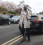 A man with sight loss walking with a long cane along a pavement, identifying a pavement edge.