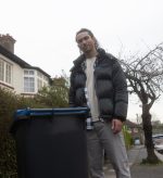 A man with sight loss stood in front of a bin on a pavement.